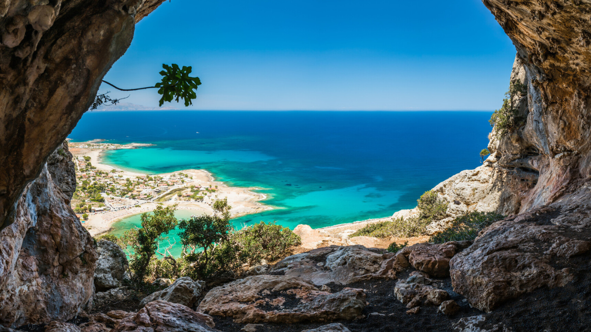 View from inside a rocky cave looking out over a tropical bay with turquoise water and a white sandy beach.