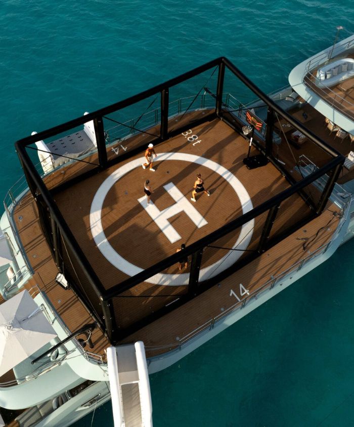 Basket ball court on the top of a blue luxury boat in clear blue waters. People playing on court.