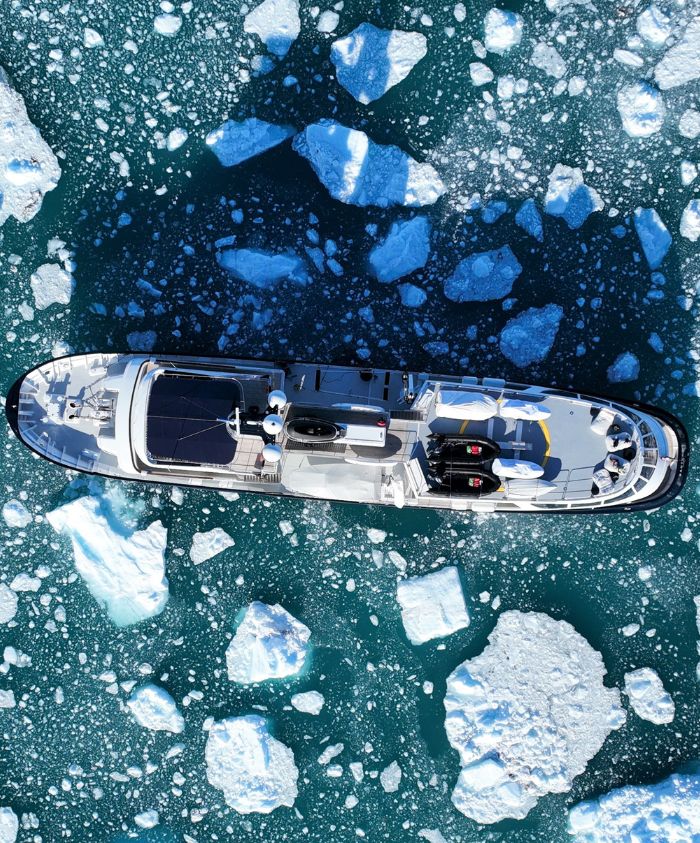 Aerial view of a large yacht navigating through icy waters, surrounded by floating icebergs.