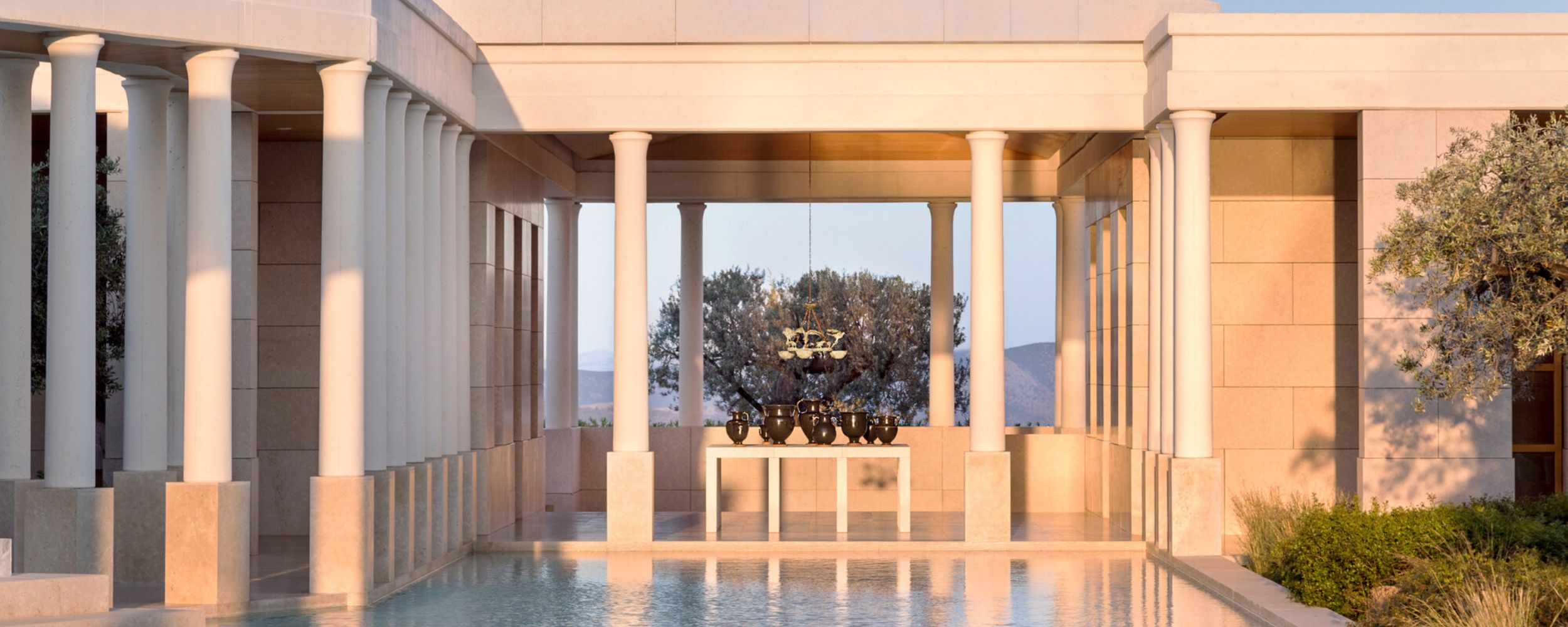 A luxurious outdoor space featuring a serene pool surrounded by elegant columns, modern architecture, and tranquil landscaping. Natural light enhances the sophisticated design and ambiance.
