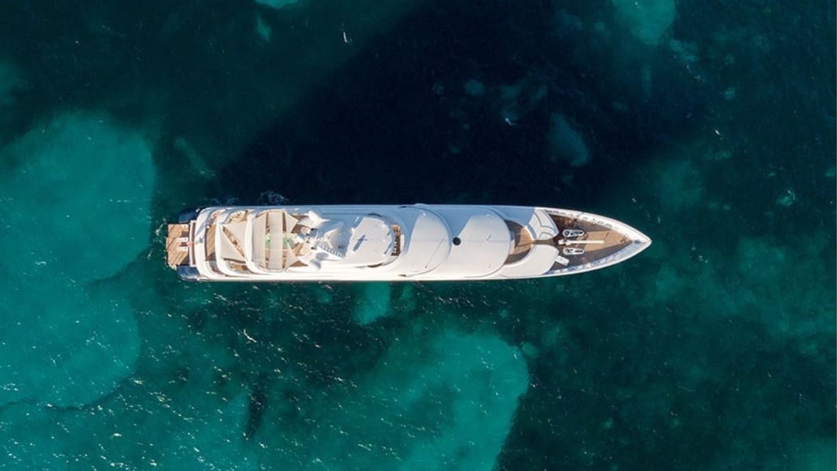 A luxury yacht with a sleek, white design anchored above turquoise waters, surrounded by clear sea.