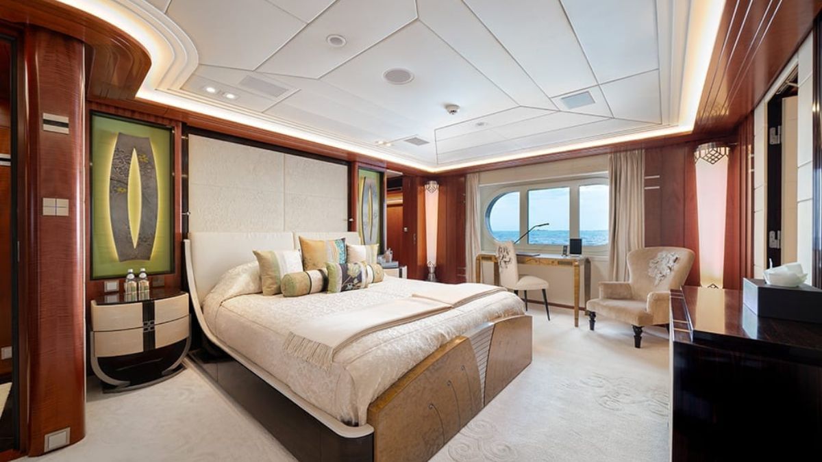 Luxurious bedroom with a large bed adorned with decorative pillows, elegant armchairs by a window, and stylish decor featuring green and gold accents. Natural light illuminates the room, highlighting its high-end finishes and ocean view.