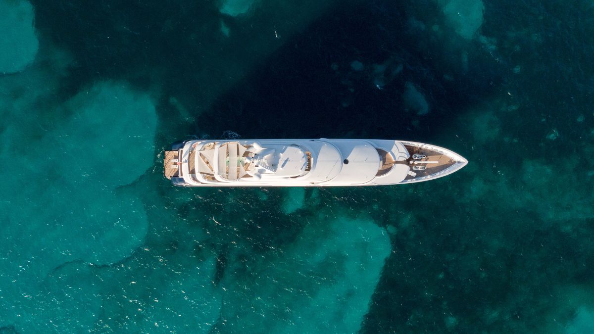 Aerial view of a luxury yacht anchored in turquoise waters, showcasing its sleek design and spacious deck areas.