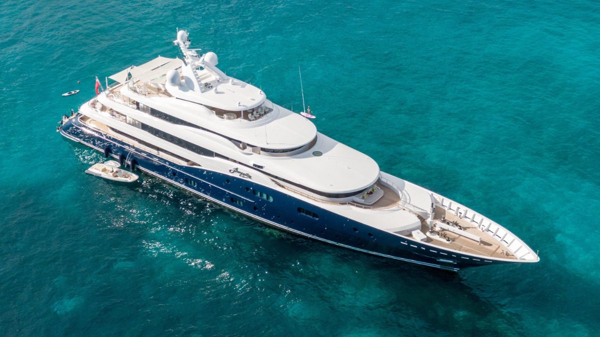 A luxurious superyacht anchored in clear turquoise waters, showcasing a sleek design with multiple decks, a helipad, and a tender alongside.