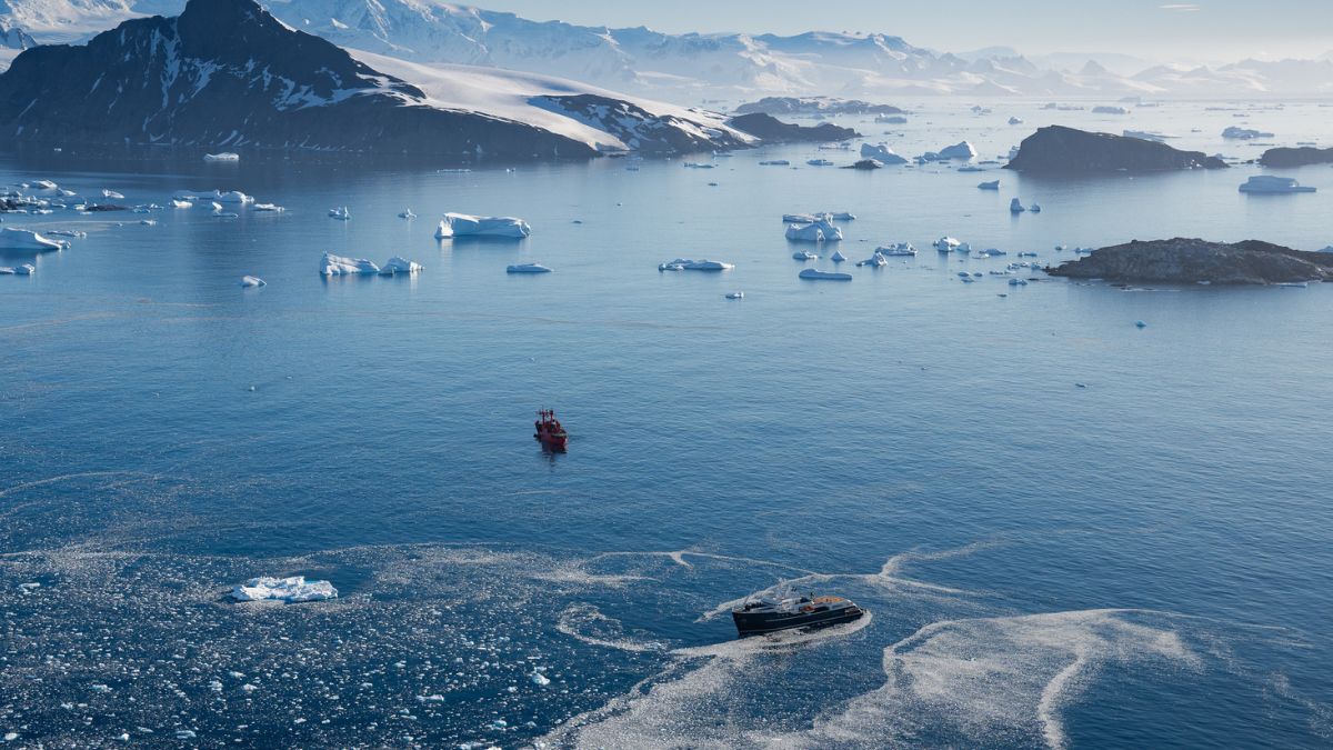Two yachts sailing in Antarctica surrounded by icebergs and snow covered mountains