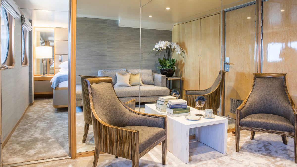 Luxurious yacht interior featuring a well-furnished lounge area with a plush sofa, two stylish armchairs, and a sleek coffee table adorned with books and decorative items. A soft carpet and elegant wall décor create a sophisticated ambience.