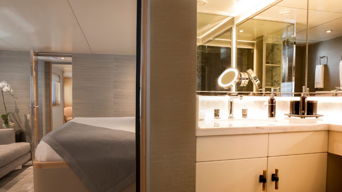 A stylish hotel room featuring a cozy bed with gray bedding, a plush armchair, and a modern bathroom with a double vanity and elegant lighting.