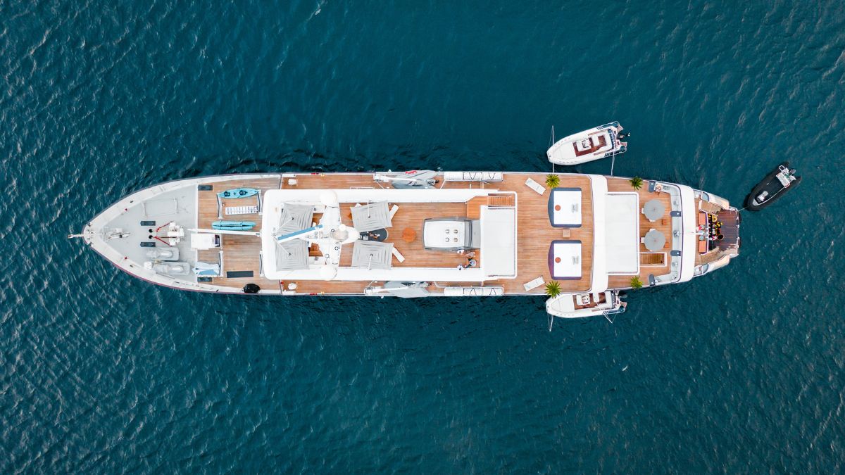 A luxurious yacht anchored in deep blue waters, featuring sun loungers, a hot tub, and multiple small boats nearby.