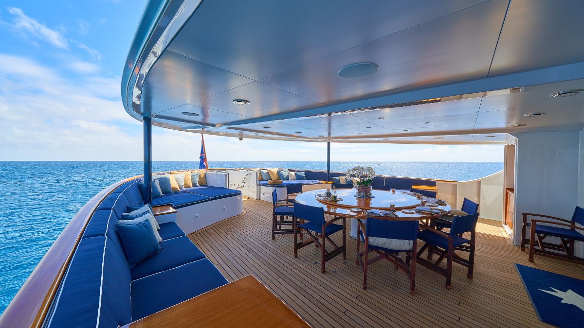 A luxurious outdoor deck with comfortable seating and a dining area, surrounded by ocean views under a clear blue sky.