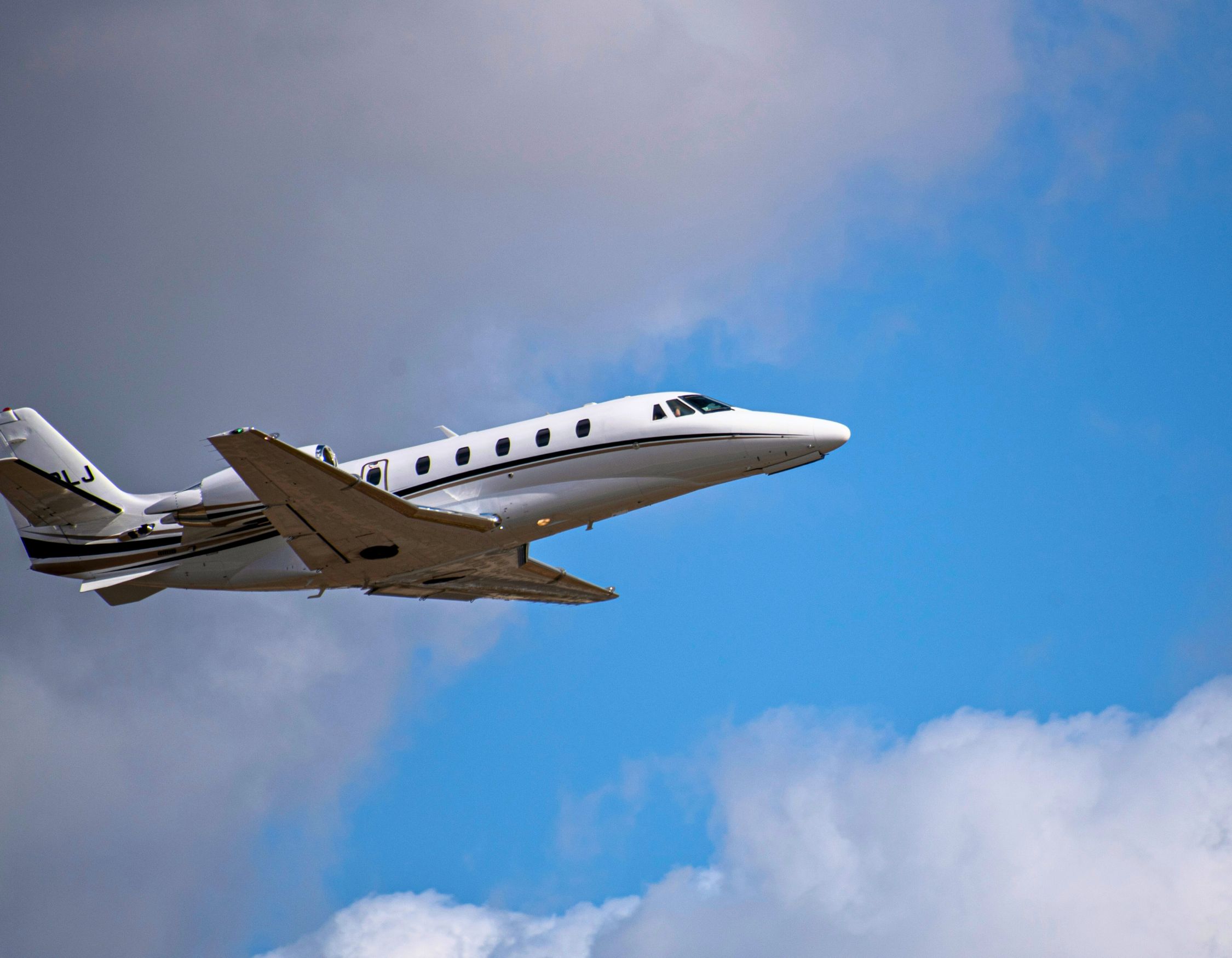 A sleek white jet flying through a partly cloudy blue sky.