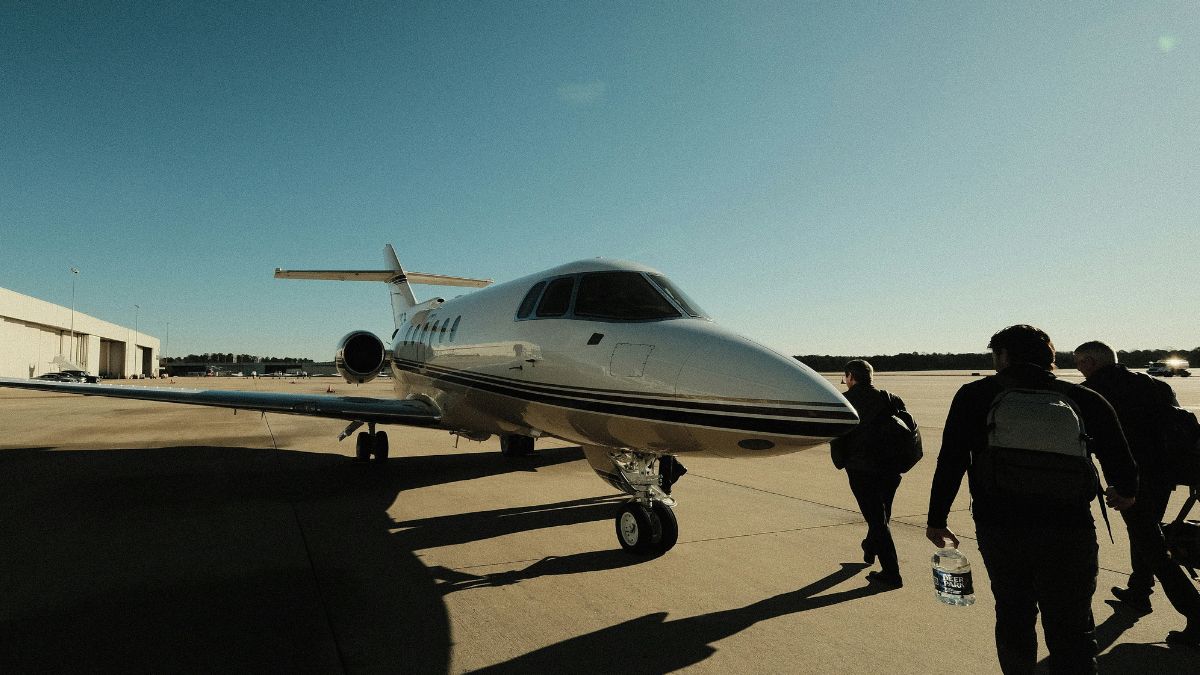 A group of people walking towards a sleek private jet on a sunny day, with a clear blue sky in the background.