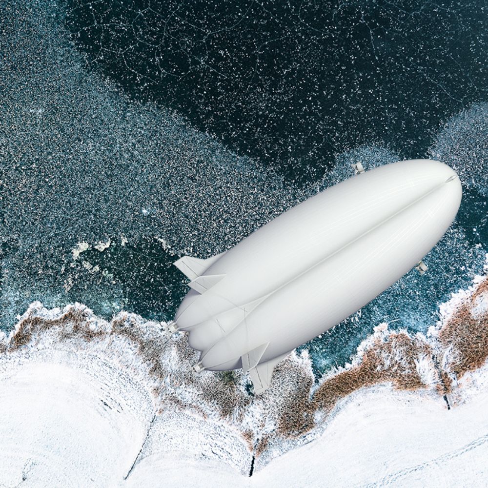 A sleek white airship hovers above a frozen shoreline, surrounded by icy waters and patches of snow.