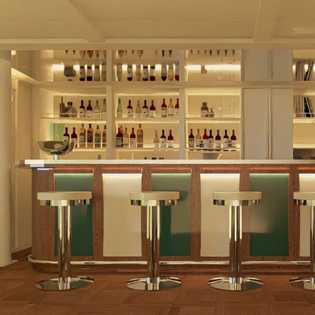 A modern bar area featuring a sleek countertop with three high stools. Behind the bar is a well-stocked shelf displaying various bottles, illuminated with soft lighting. The design incorporates wood and green accents.
