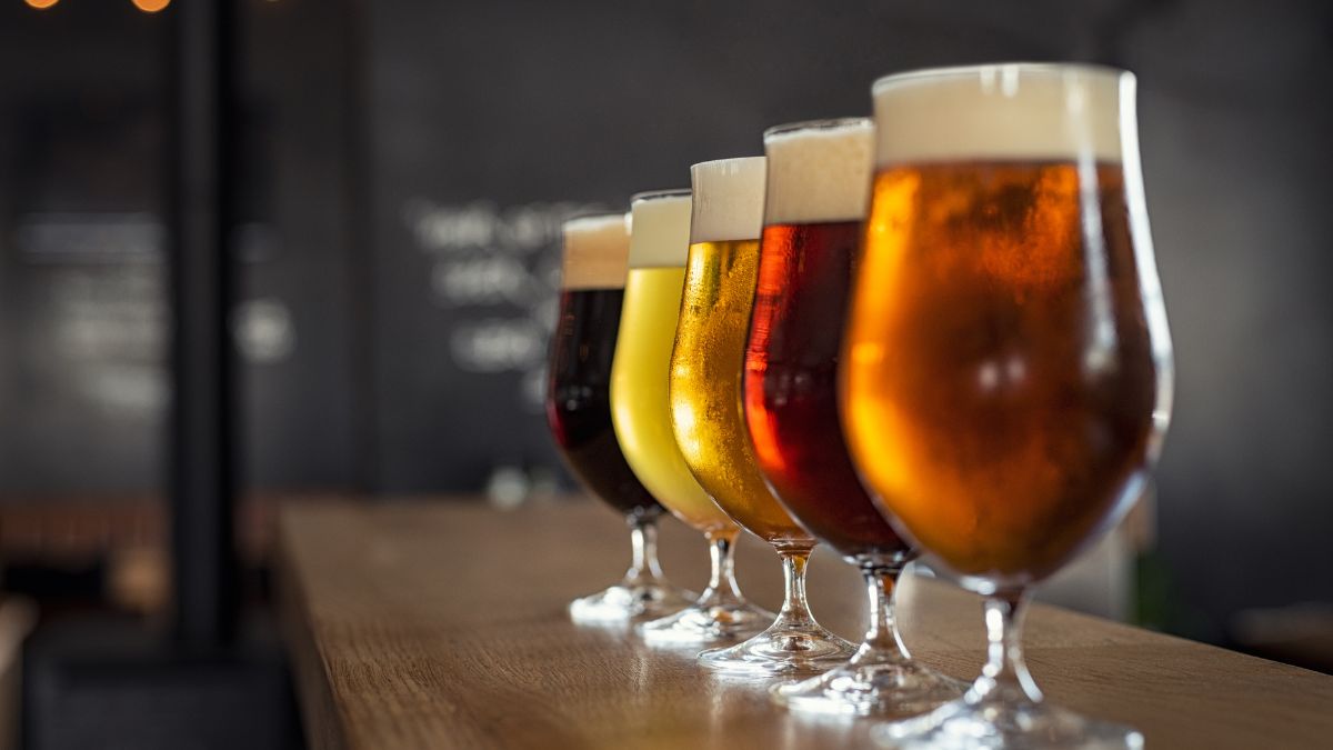 A row of five glasses filled with different types of beer, showcasing various shades from light yellow to deep brown, all with frothy tops.