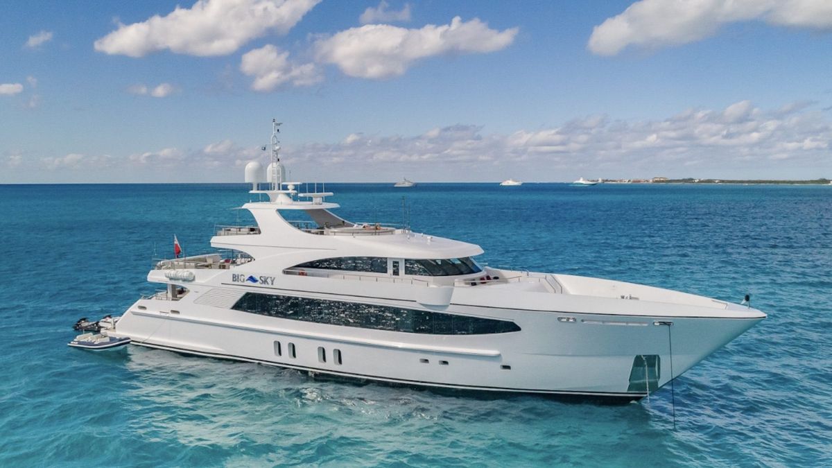 A sleek white luxury yacht navigates through clear turquoise waters under a blue sky with scattered clouds.