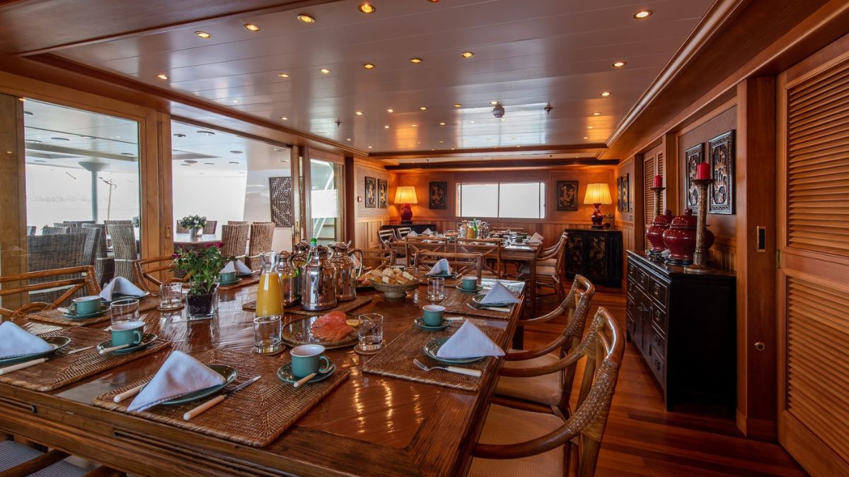 A beautifully arranged dining area with wooden furniture, elegant table settings, and decorative elements. The room features large windows allowing natural light, with comfortable seating and tasteful decor, creating a warm and inviting atmosphere.