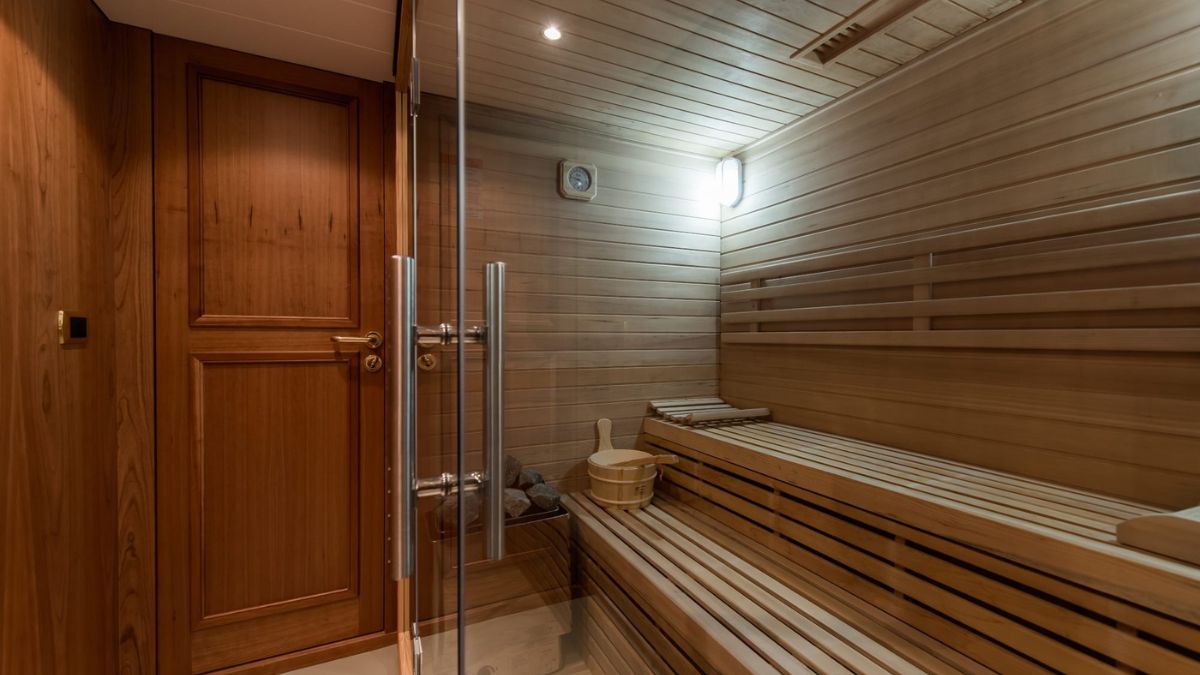 A modern wooden sauna featuring bench seating, a thermometer on the wall, and soft lighting. The entrance is through a glass door.