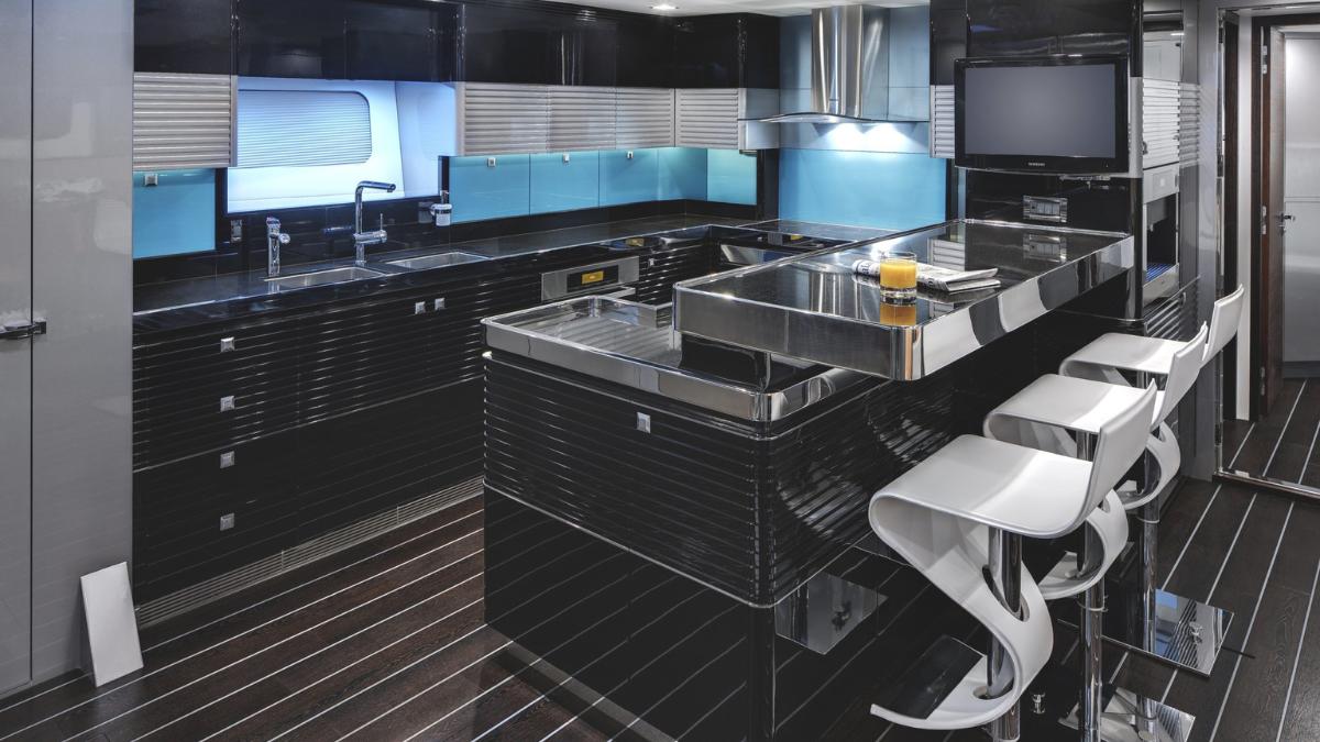 Modern kitchen design featuring sleek black cabinetry, a central island with a breakfast bar, and stainless steel appliances. The space is illuminated with blue backlighting, giving it a contemporary feel. Stylish white bar stools are arranged around the island.