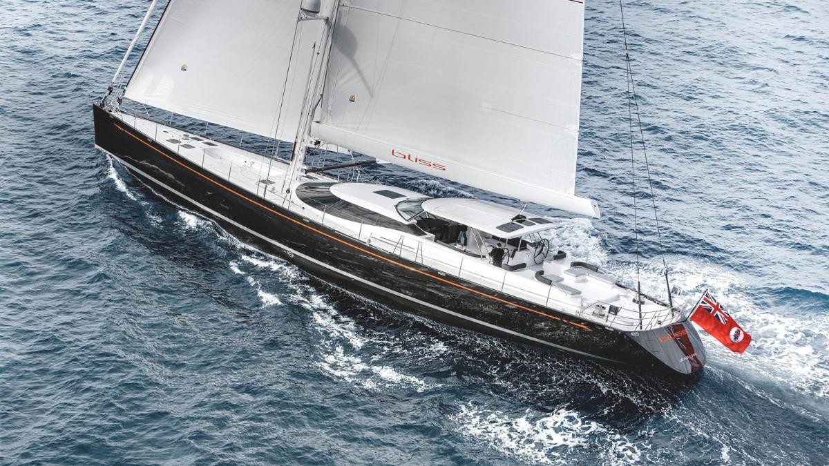 A sleek sailboat with a black hull and white sails glides through blue waters, flying a red and white flag at the stern.