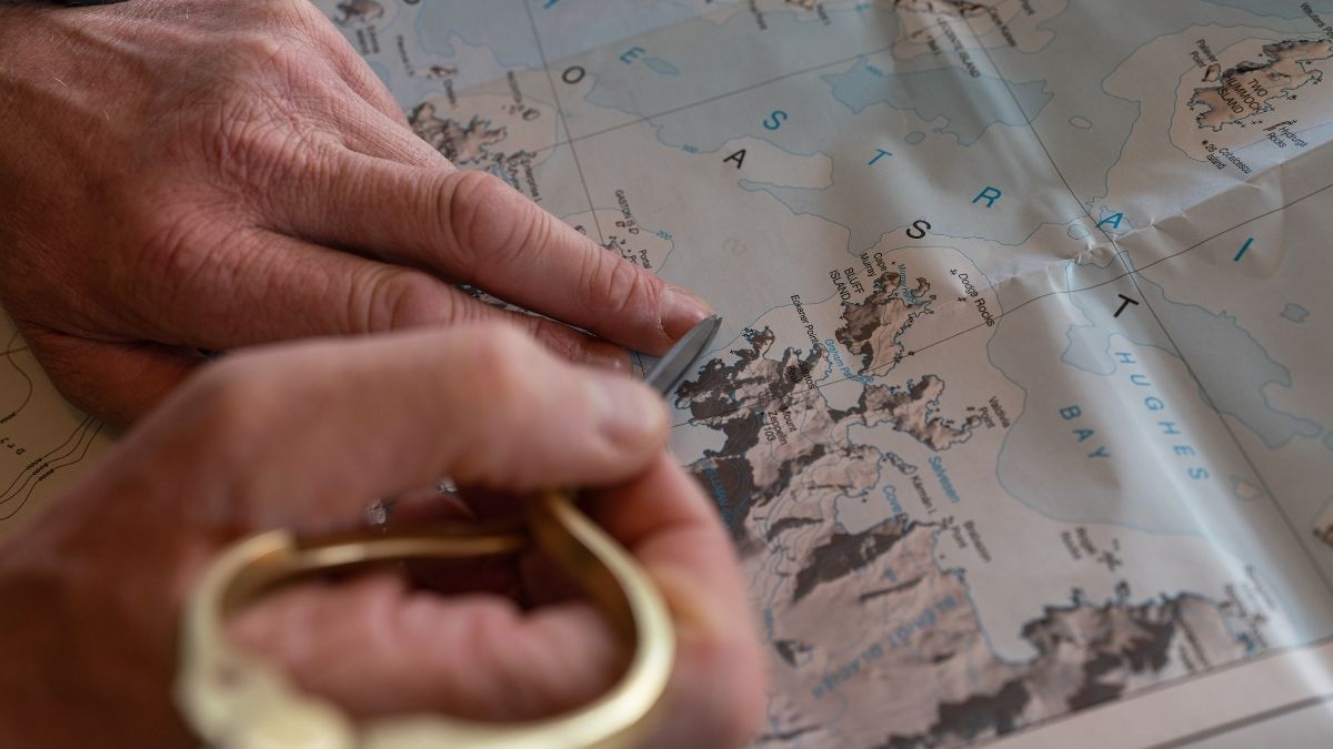 A close-up of hands holding a ruler against a geographical map, highlighting a specific location near water and coastal features.