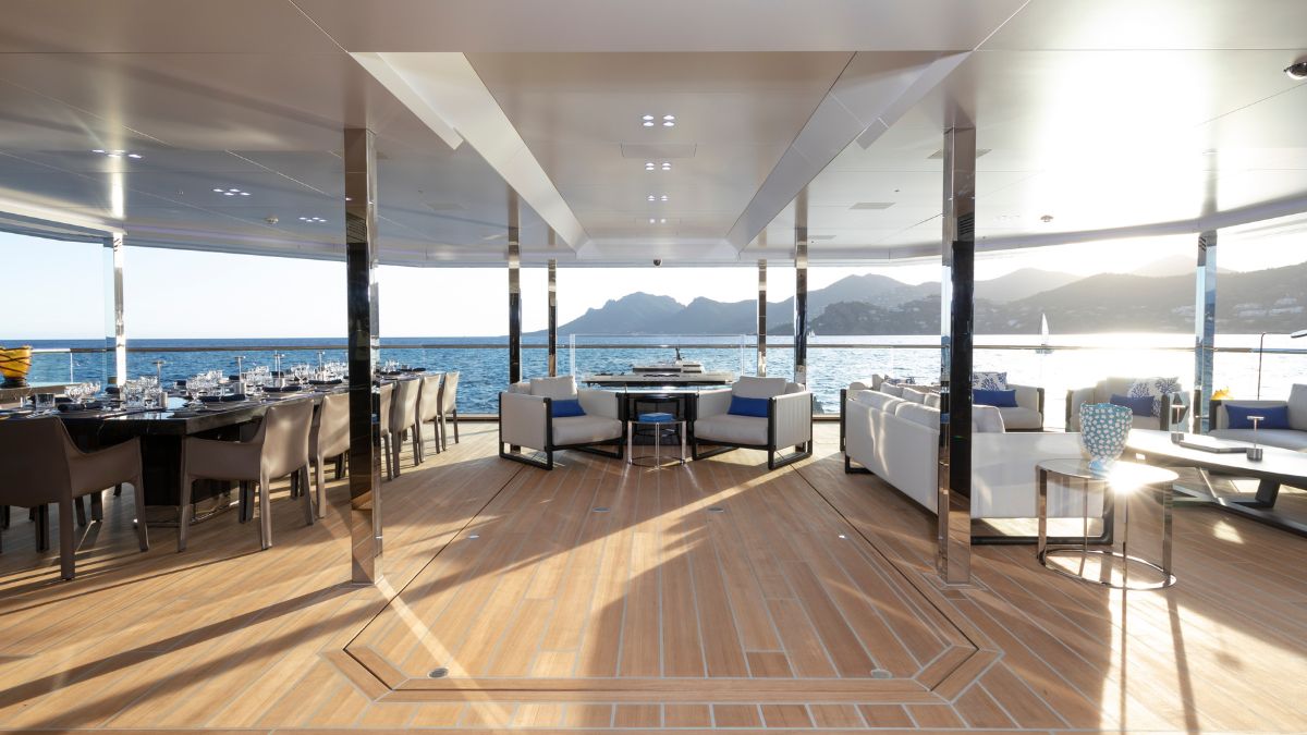 Luxurious dining area on a yacht with elegant tables and chairs, large windows offering a panoramic view of the sea and mountains. Stylish decor and soft lighting create a sophisticated atmosphere.