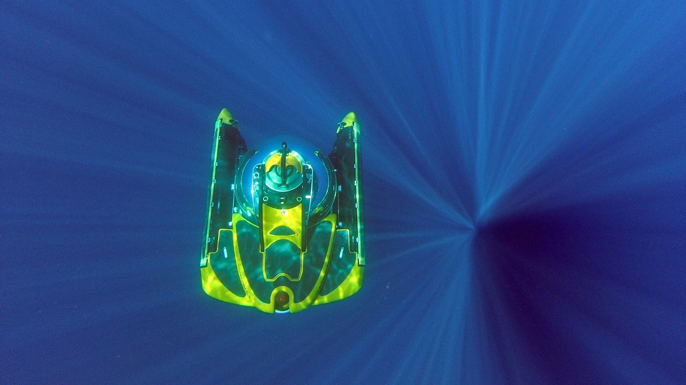 A brightly colored submersible is gliding through deep blue water, surrounded by rays of light creating a starburst effect.