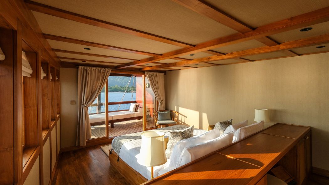 A cozy bedroom featuring wooden accents, large windows with scenic views, and soft lighting. There are two beds with decorative pillows, a small seating area, and a workspace.