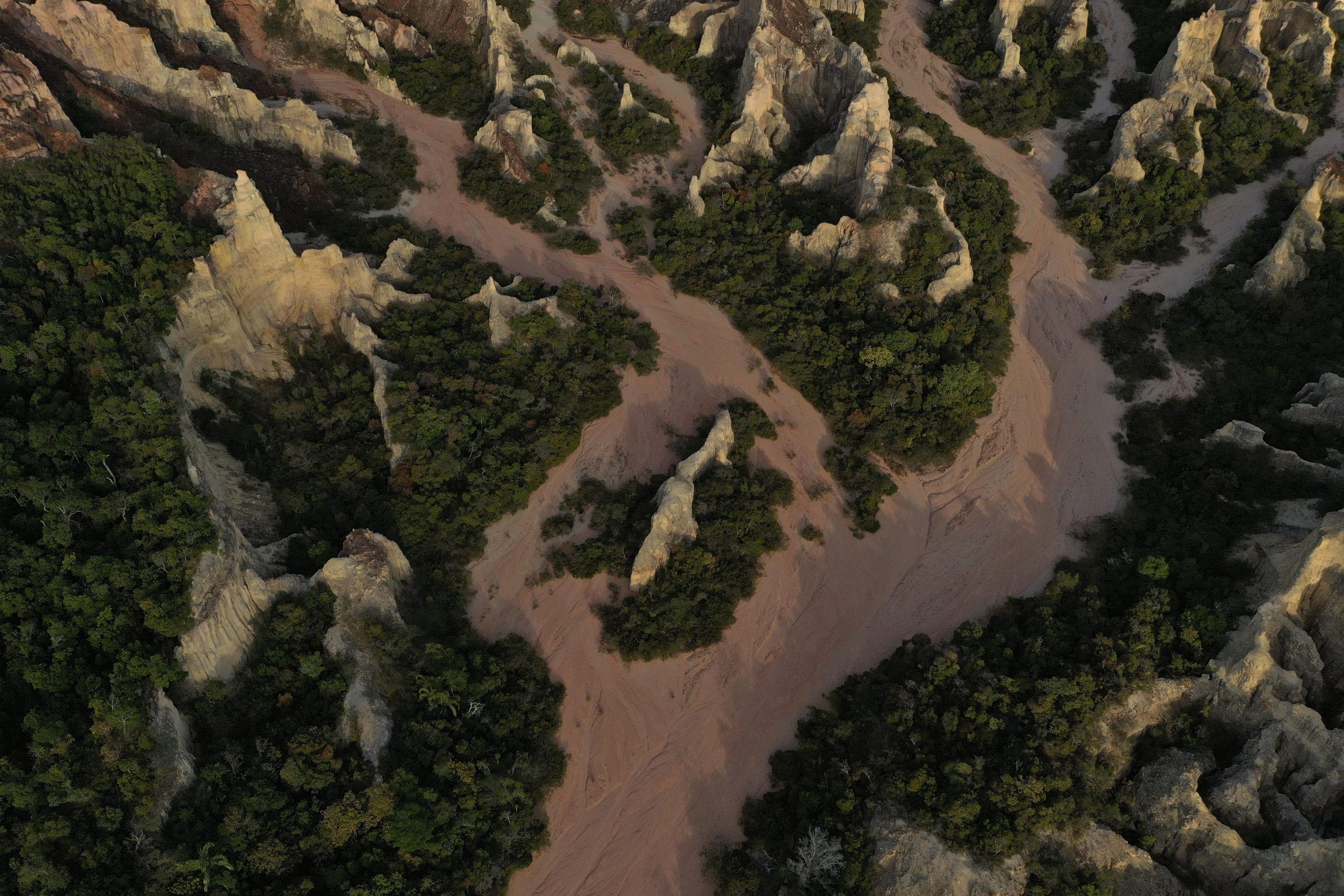 Aerial view of rugged terrain featuring tall rock formations surrounded by lush greenery and sandy paths winding through the landscape.