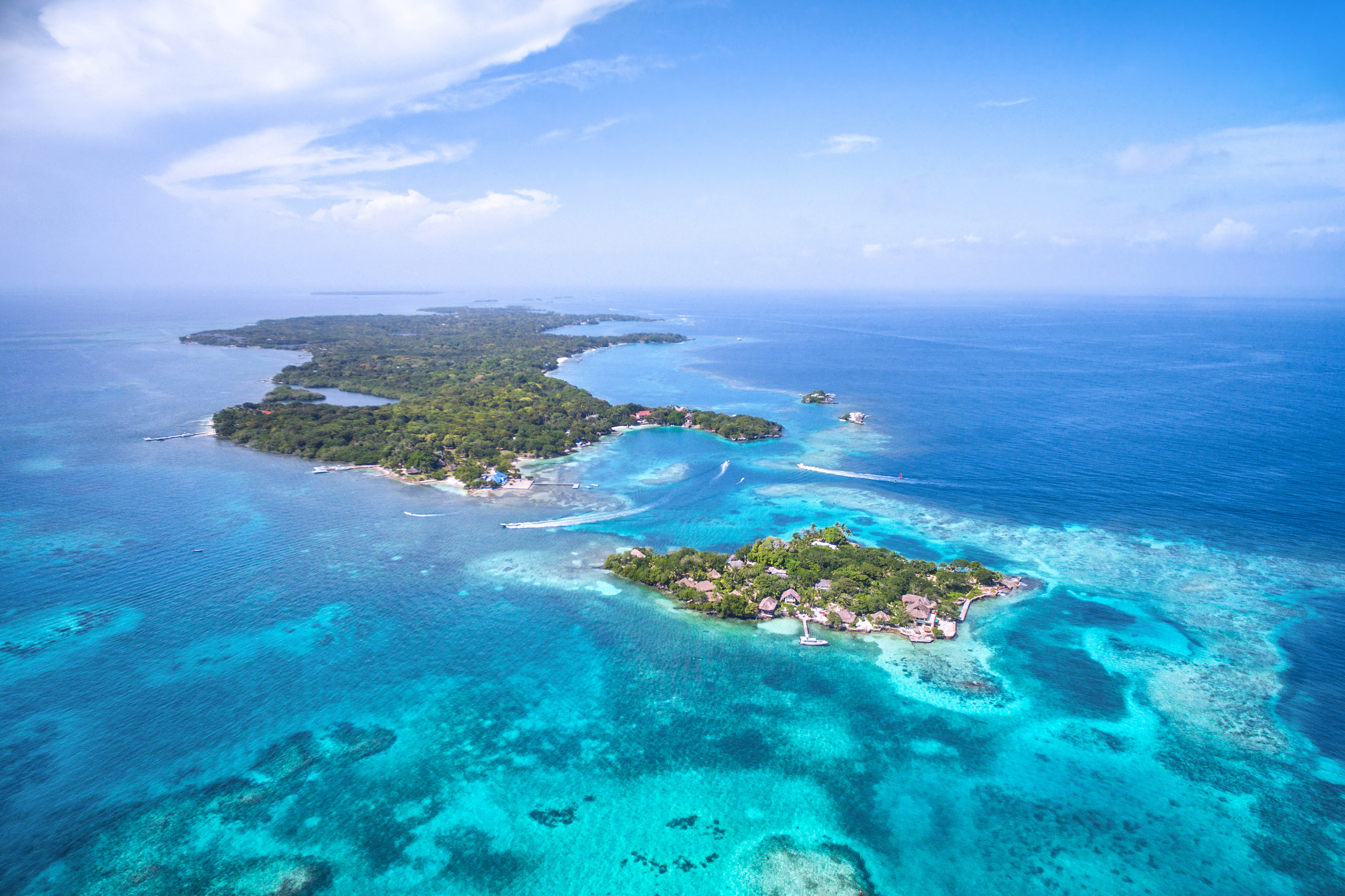Aerial view of a tropical island surrounded by vibrant turquoise waters and lush greenery, with small boats and white sand beaches visible throughout the landscape.