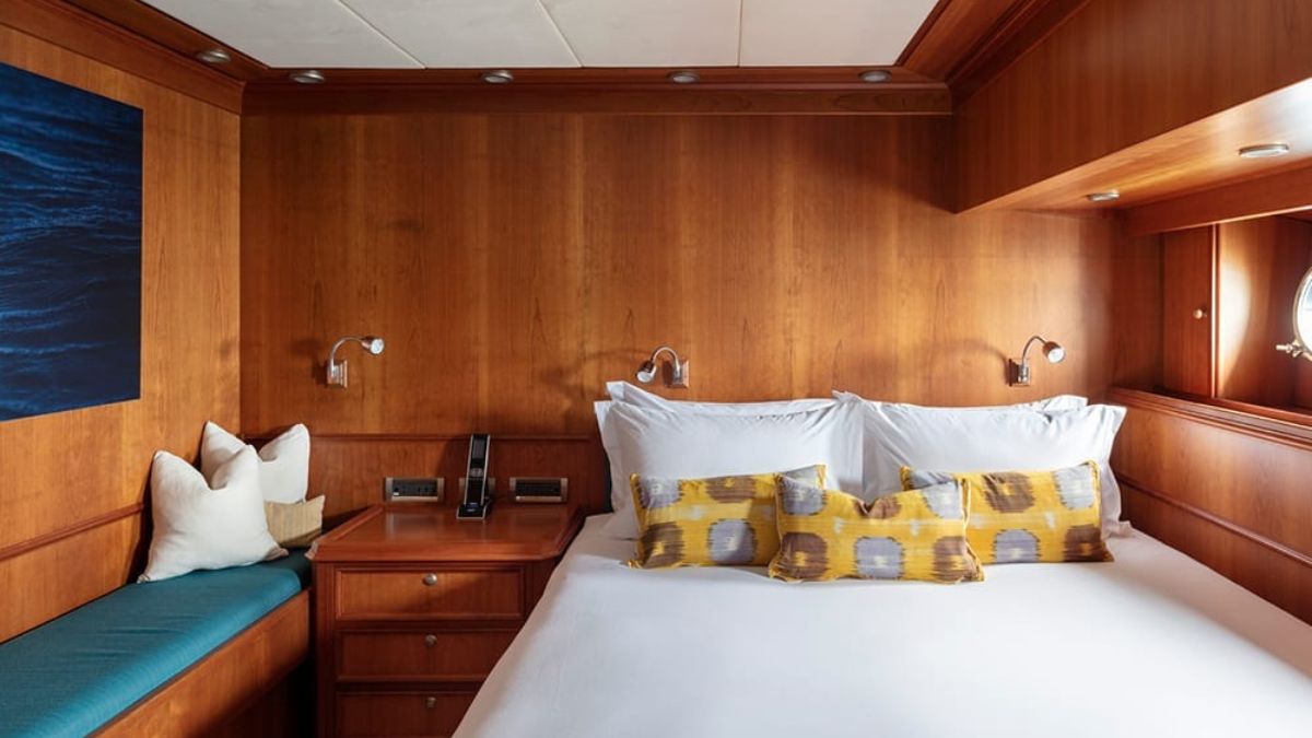 Cozy cabin interior featuring a queen-sized bed with decorative pillows, wooden paneling, bedside lamps, and a small seating area by the window.