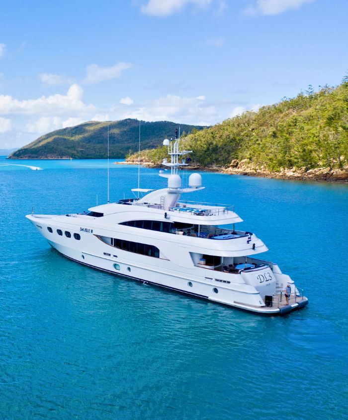 A sleek white yacht anchored in a turquoise bay, surrounded by lush green hills and clear blue skies.