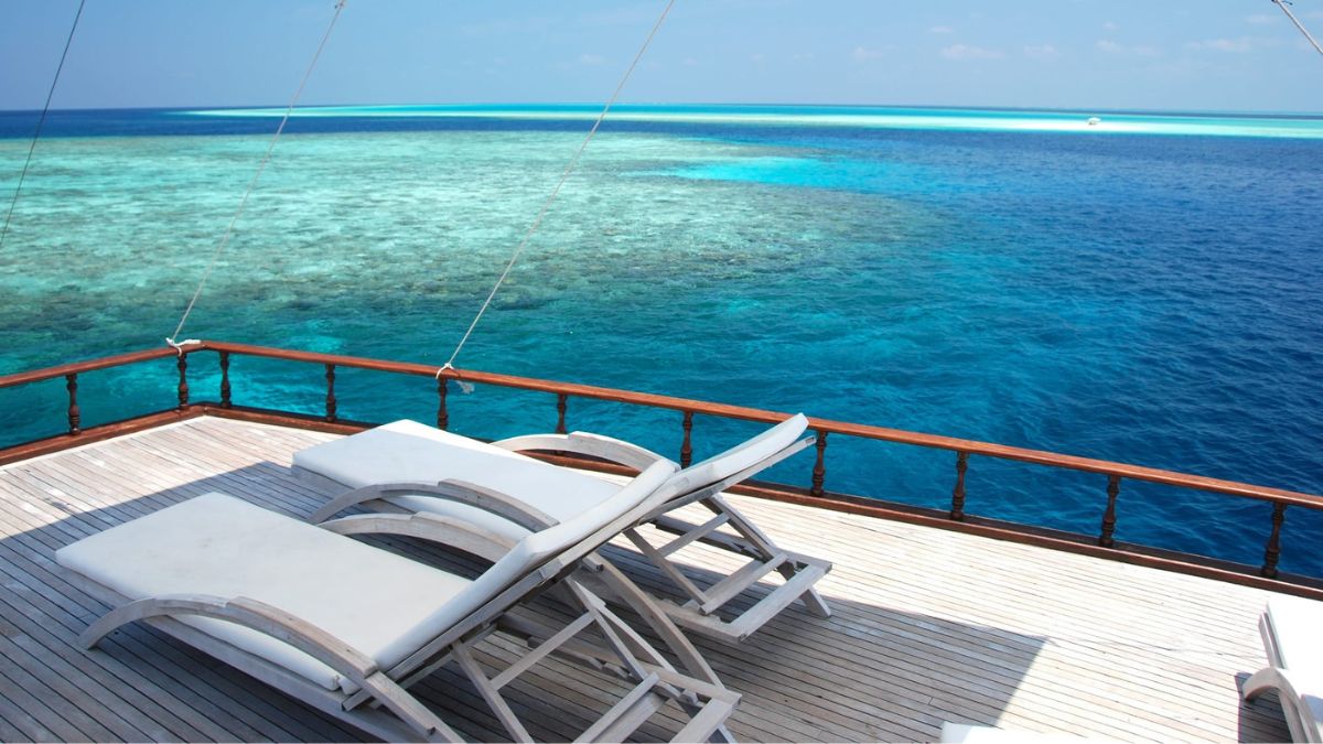 Lounge chairs on a wooden deck overlooking crystal clear turquoise waters and a vibrant coral reef.
