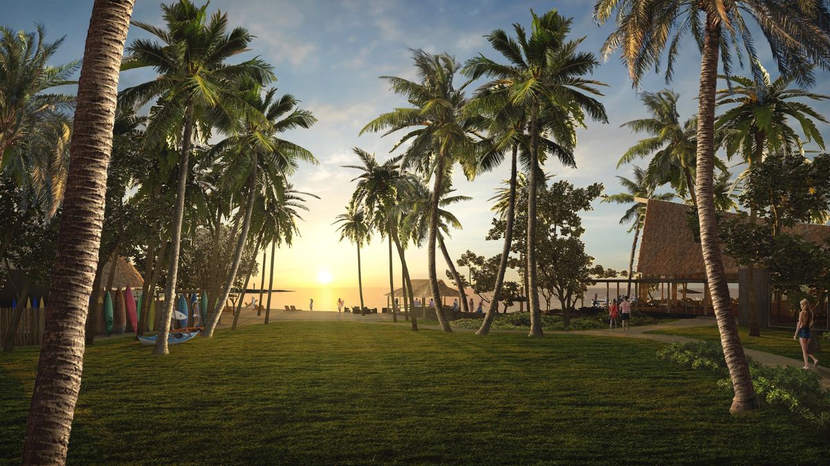 A tropical landscape with tall palm trees lining a grassy area, leading towards the ocean at sunset. People can be seen in the distance, enjoying the beach. Simple beach huts and equipment are visible along the shore. The sky is partially cloudy, creating a warm, inviting atmosphere.