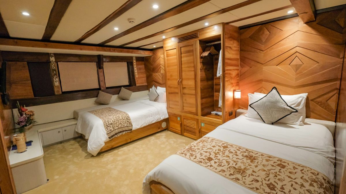 A cozy hotel room featuring two beds with decorative throw blankets. Wooden walls with a geometric pattern surround the space, and a wardrobe is built into the side. Soft lighting enhances the warm atmosphere.