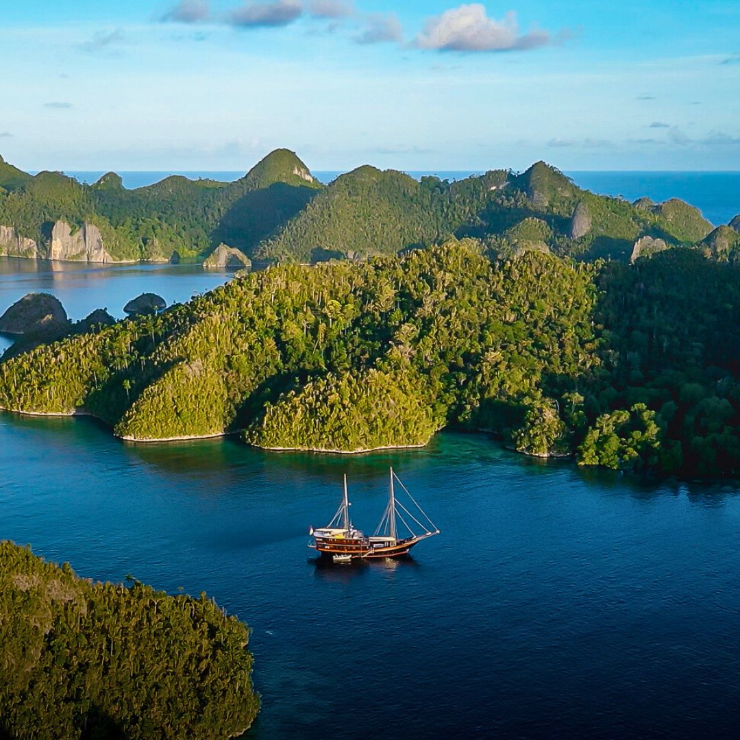 A traditional wooden boat anchored in a calm blue bay surrounded by lush green islands and hills under a clear sky.