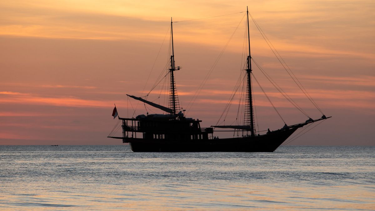 A silhouette of a traditional sailing ship against a colorful sunset over calm waters.