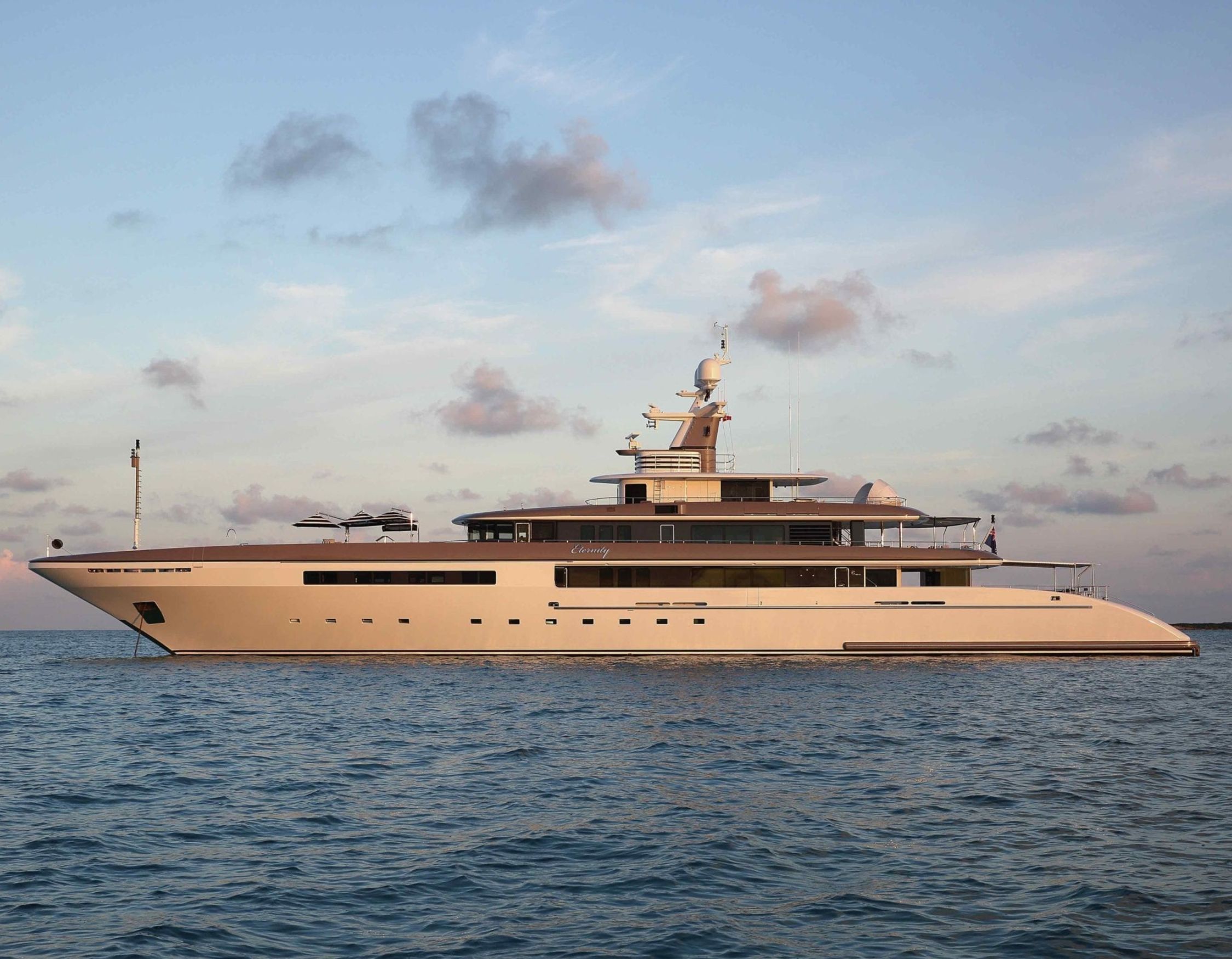 A luxurious yacht anchored on calm waters, showcasing a sleek, modern design with multiple decks and elegant lines under a partly cloudy sky.