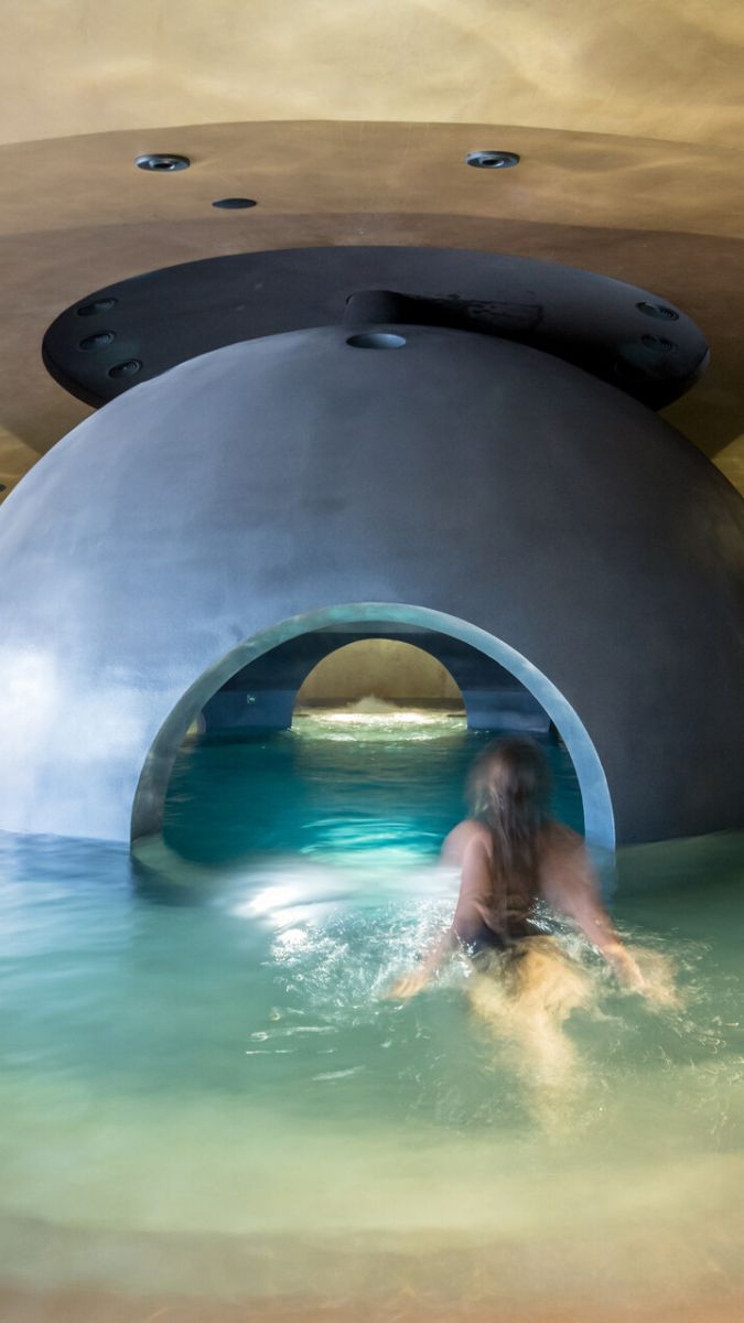 A person wading through a tranquil water area inside a modern architectural structure, featuring a large curved dome and gentle lighting.