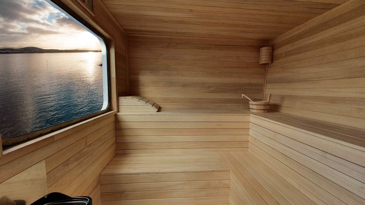 A wooden sauna interior with smooth benches, a sleek corner seat, and a large window revealing a serene view of the water and sky outside.