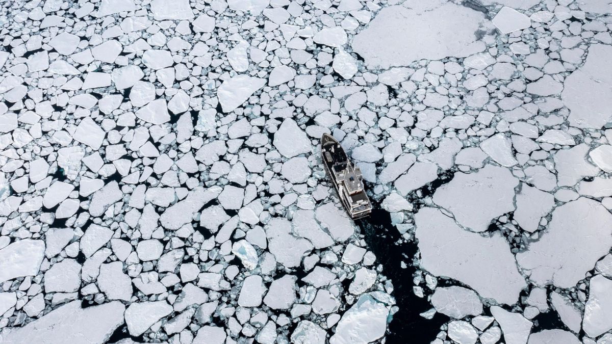 A ship navigates through a sea of broken ice, creating a narrow channel through the jagged ice formations.