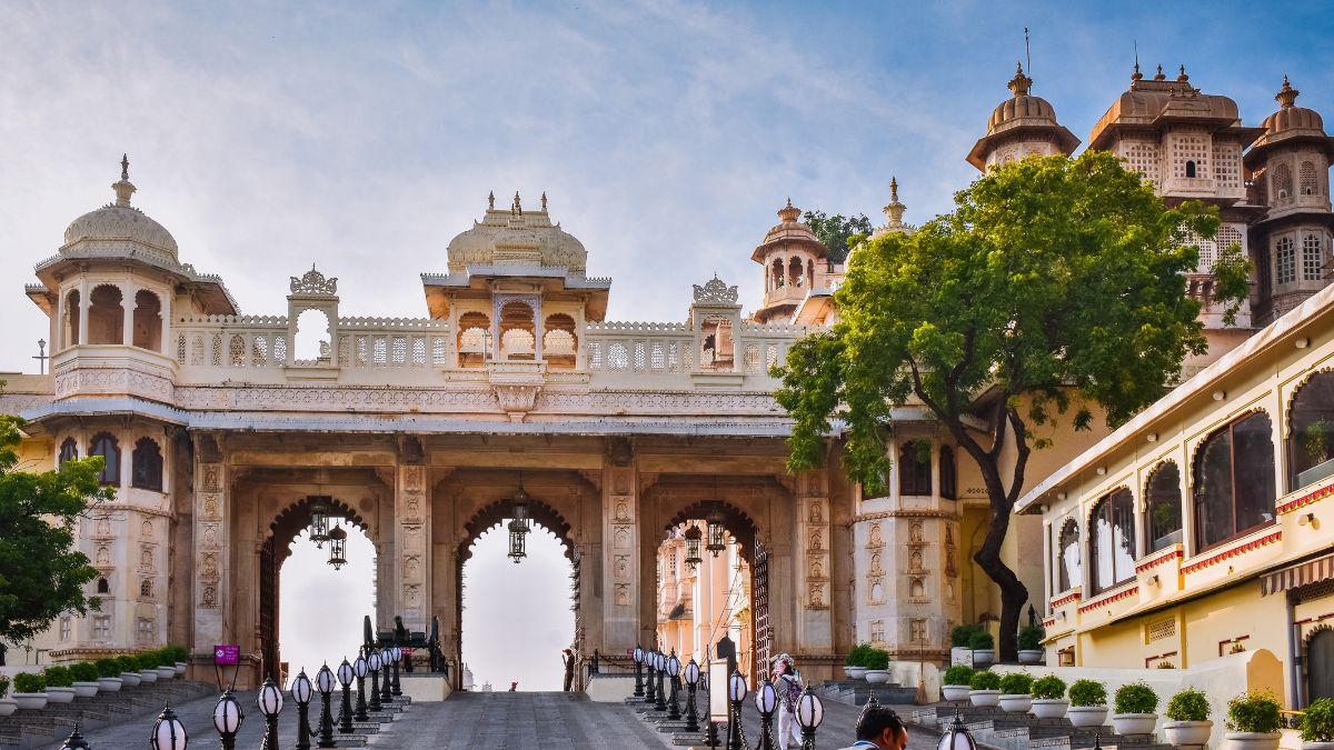 A grand entrance featuring intricate architectural details and arches, surrounded by lush greenery. The structure combines traditional design with ornate carvings and domes against a clear blue sky.