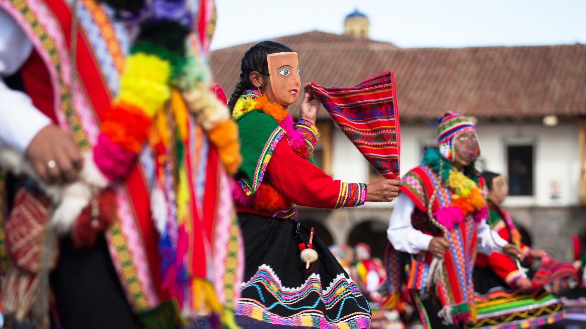 Participants in traditional colorful costumes and masks dancing at a festival in a vibrant outdoor setting.