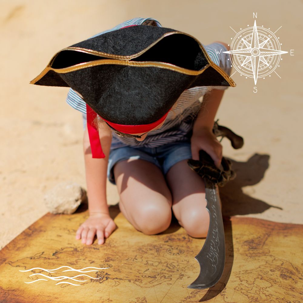 A child dressed as a pirate examines a treasure map on the ground, wearing a tricorn hat and holding a toy sword. A compass and wave graphic are in the corners.
