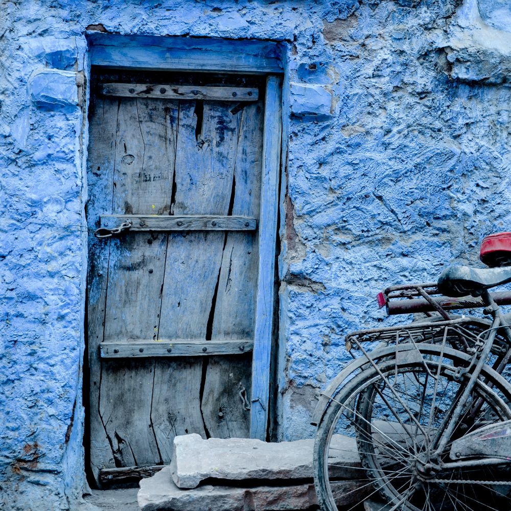 A weathered wooden door stands against a blue-stucco wall, with a rustic bicycle leaning beside it.