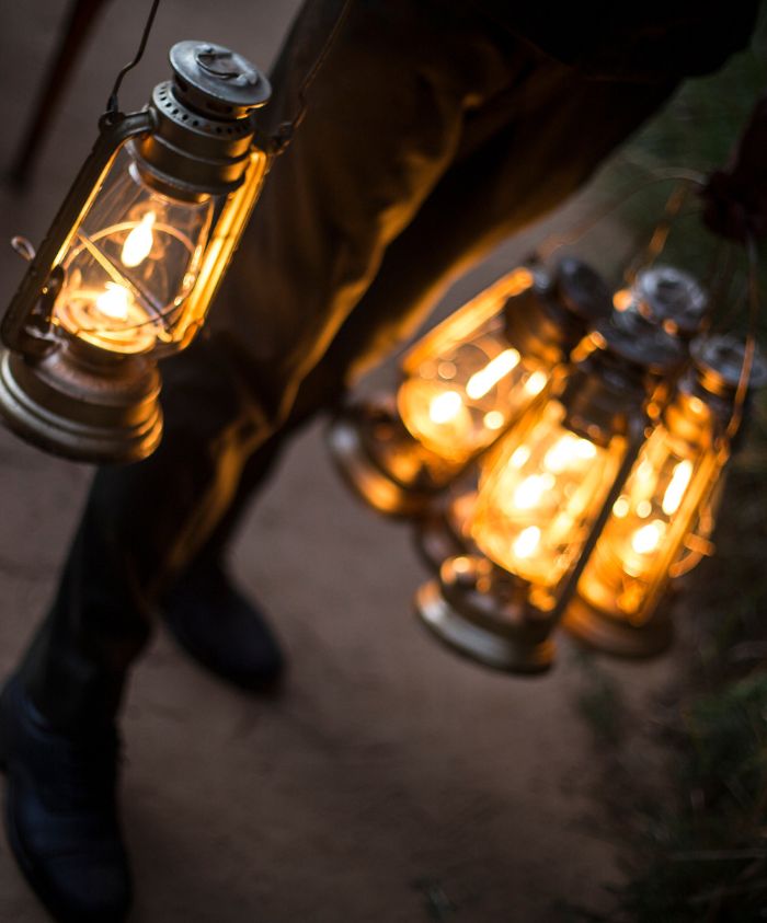 A person holds multiple glowing lanterns, their warm light illuminating the surrounding area. The scene conveys a cozy, inviting atmosphere.