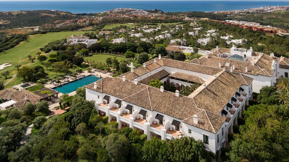 Aerial view of a luxurious resort surrounded by lush greenery and a golf course, with swimming pools and coastal scenery in the background.