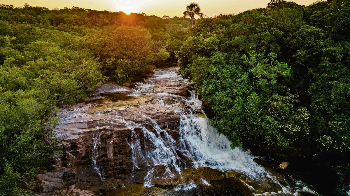 A serene waterfall cascading over rocky terrain, surrounded by lush greenery and bathed in the warm glow of a sunset.