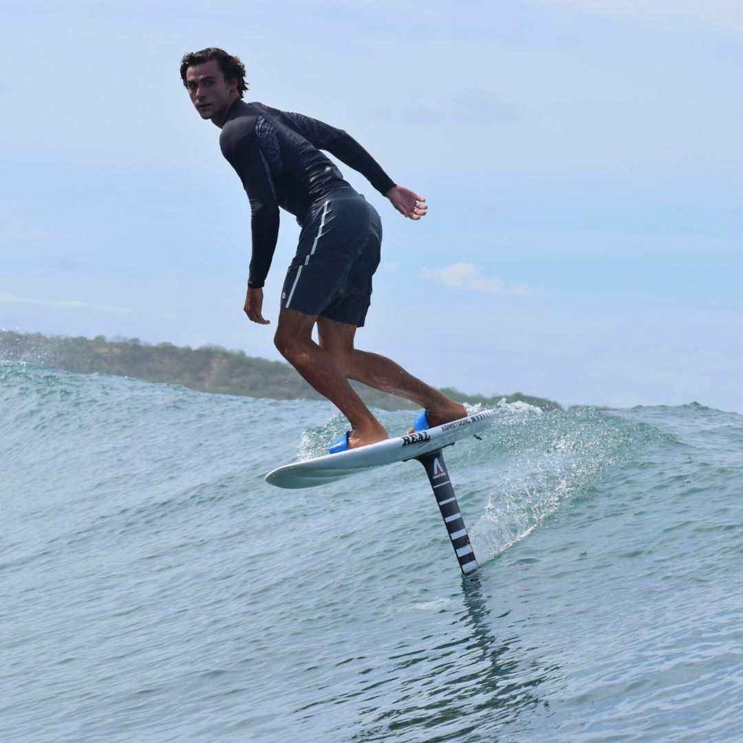 A surfer glides above the water on a hydrofoil board, skillfully balancing as he rides a wave in a sunny ocean setting.