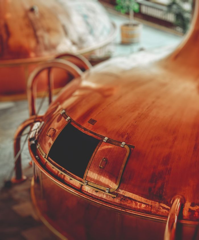 Copper brewing kettles with shiny surfaces and open hatches, positioned in a brewery setting.