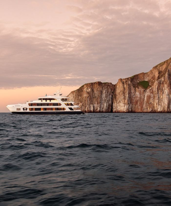 Luxury superyacht navigating near iconic Galápagos rock formations for a luxury yacht charter adventure.
